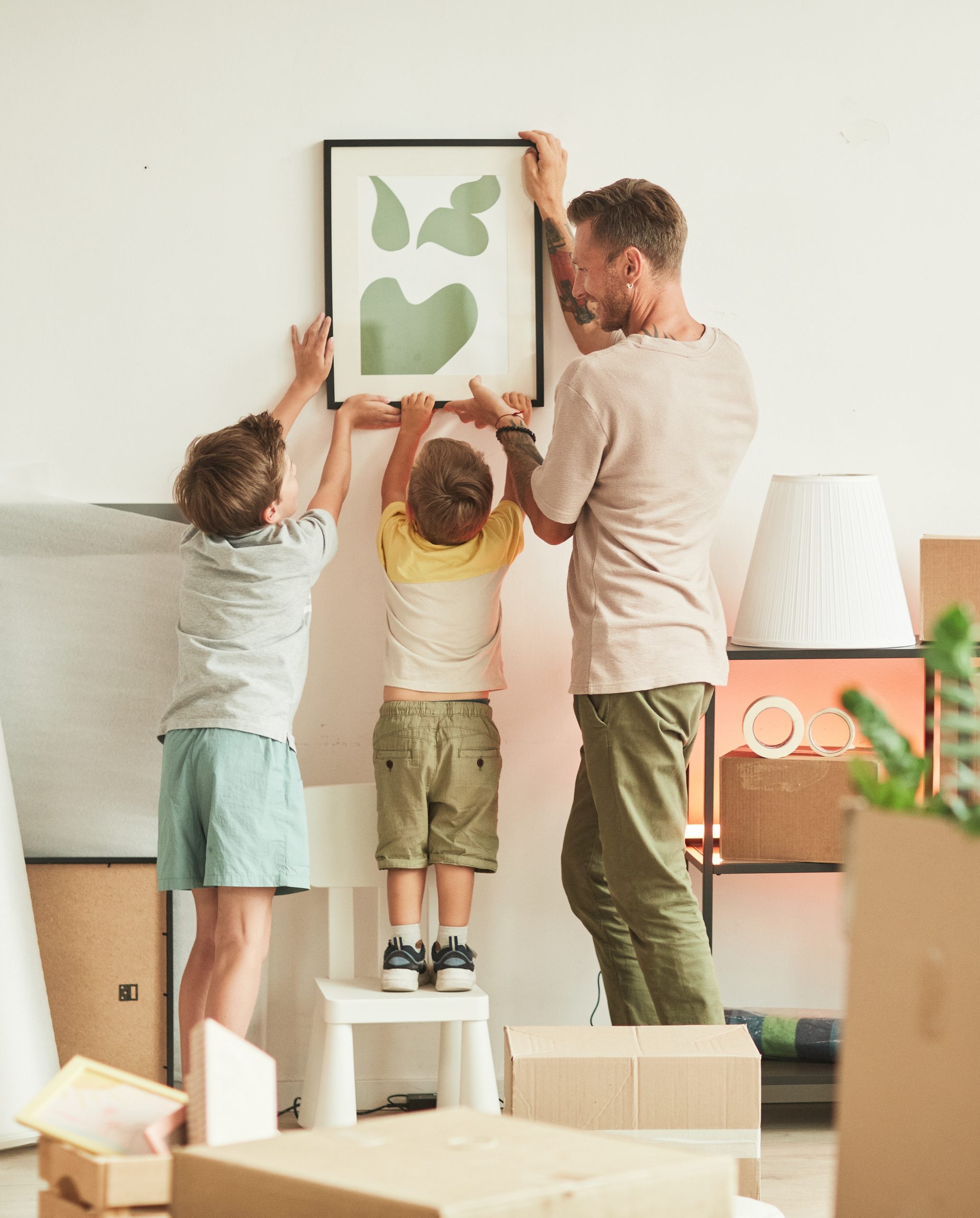 Pere et ses enfants accrochent un cadre dans leur nouveau bien immobilier