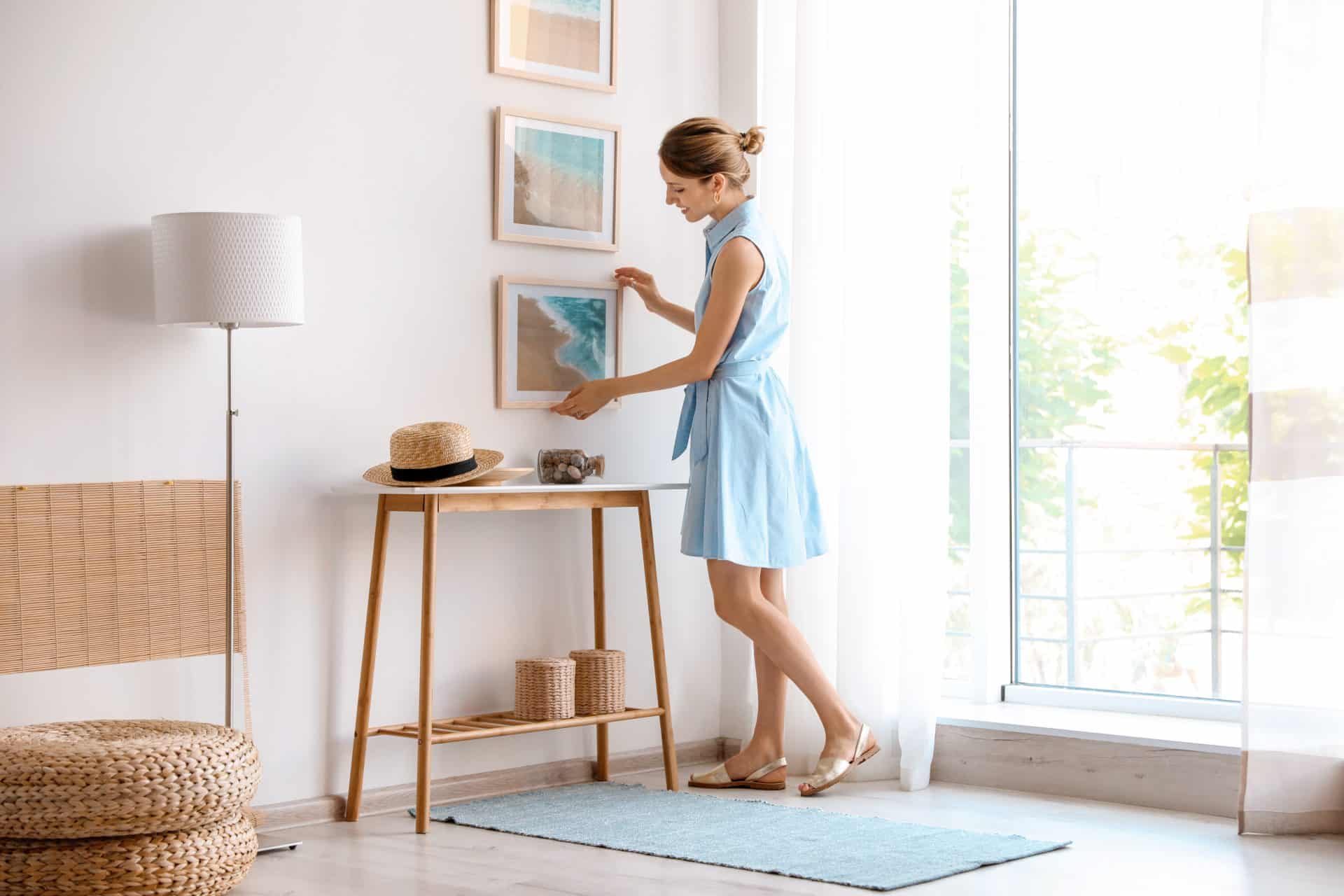 Femme qui accroche un cadre dans son salon pour décorer sa maison lors d'un home staging
